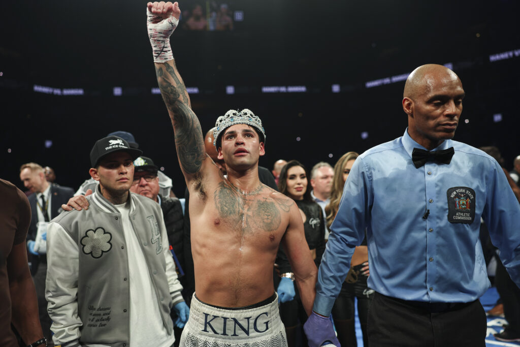 Ryan Garcia raises his fist while wearing a crown and standing next to a referee