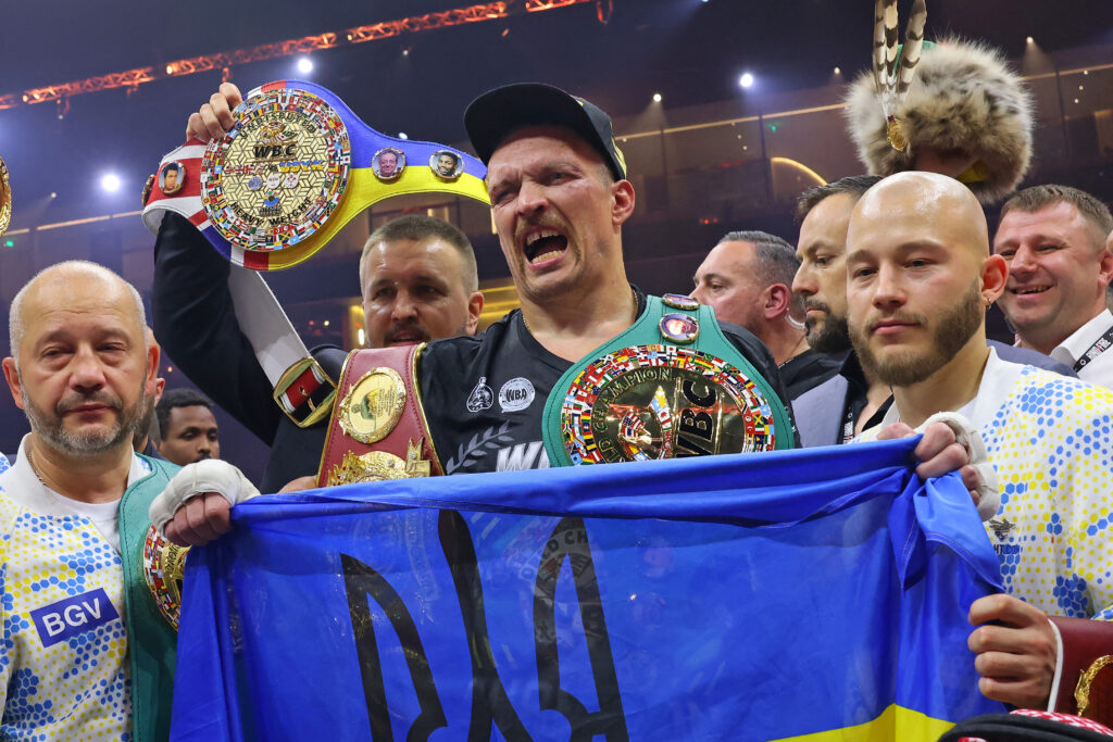Oleksandr Usyk holds a Ukraine flag while celebrating with his team and all of his belts after beating Tyson Fury