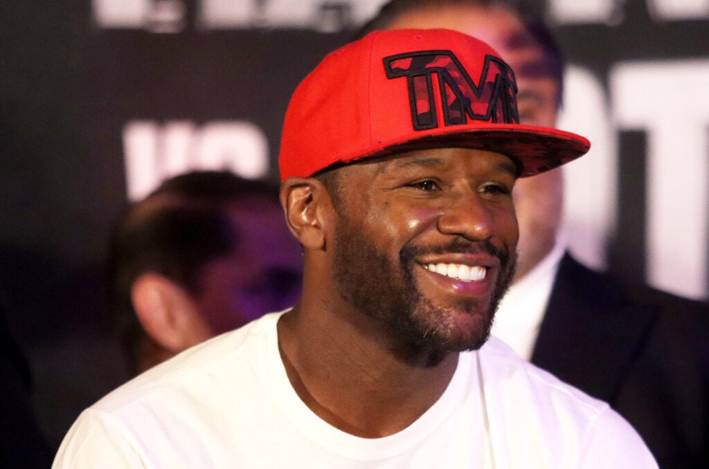 Floyd Mayweather smiling while wearing a red hat before the weigh in for his fight against John Gotti III