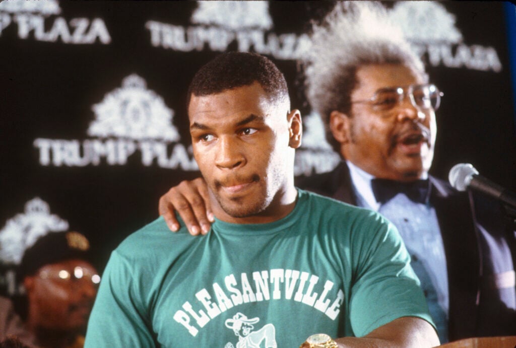 Mike Tyson in a green t shirt stood beside Don King, who has his arm around him, at the press conference before Tyson vs Spinks in 1988