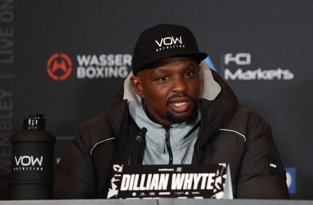 Dillian Whyte sitting in jacket and hat at a press conference