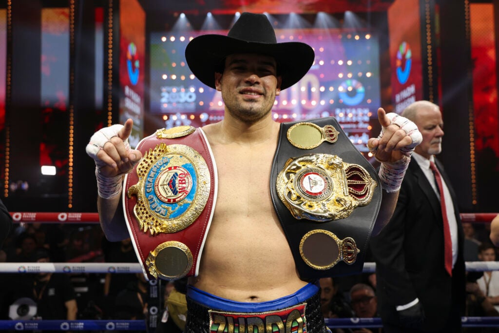 Gilberto "Zurdo" Ramirez poses with a cowboy hat on and belts over his shoulders after beating Chris Billam-Smith