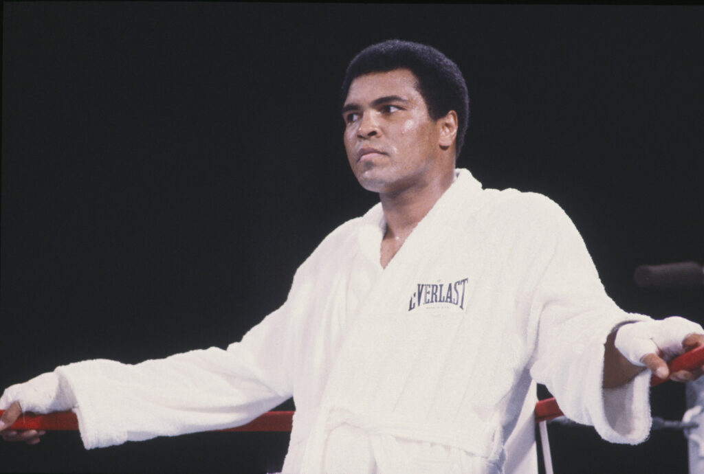 Muhammad Ali stood in a robe against the corner of the ring