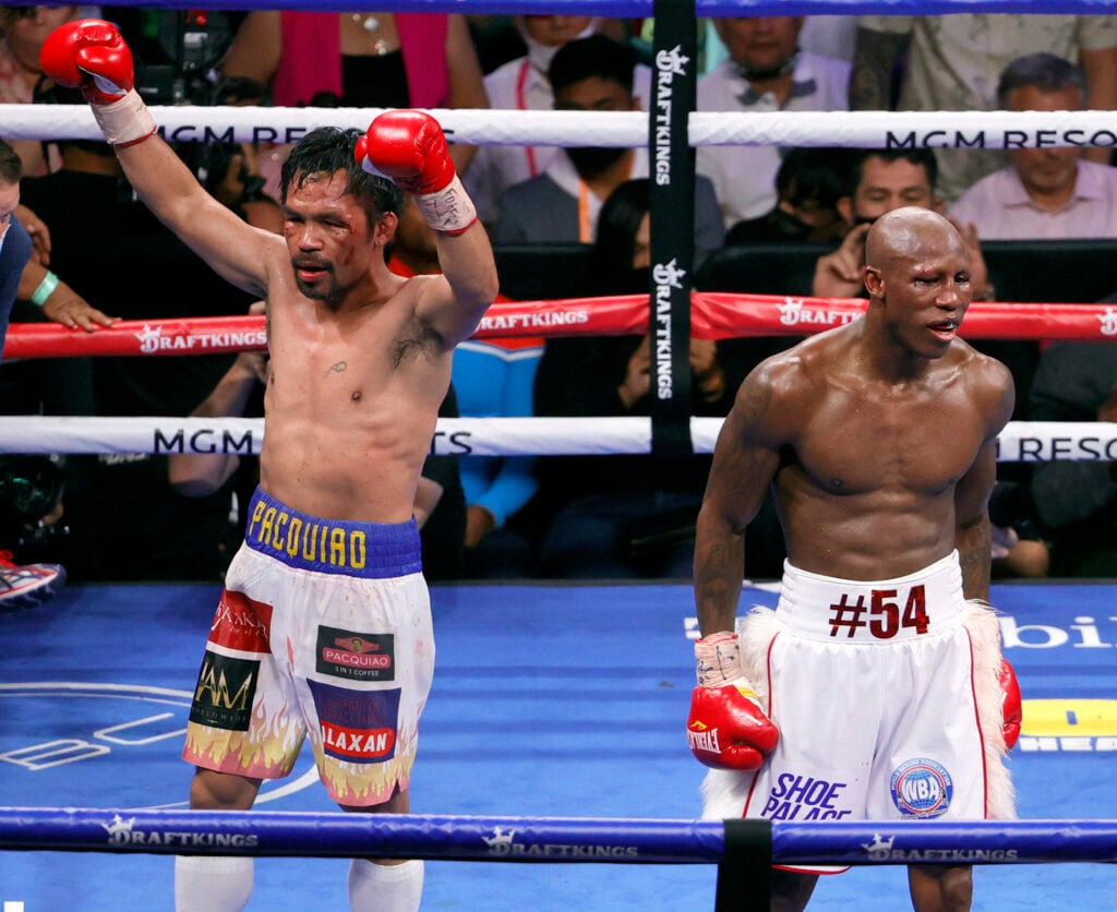 Yordenis Ugás walks off as Manny Pacquiao raises his hands after their fight
