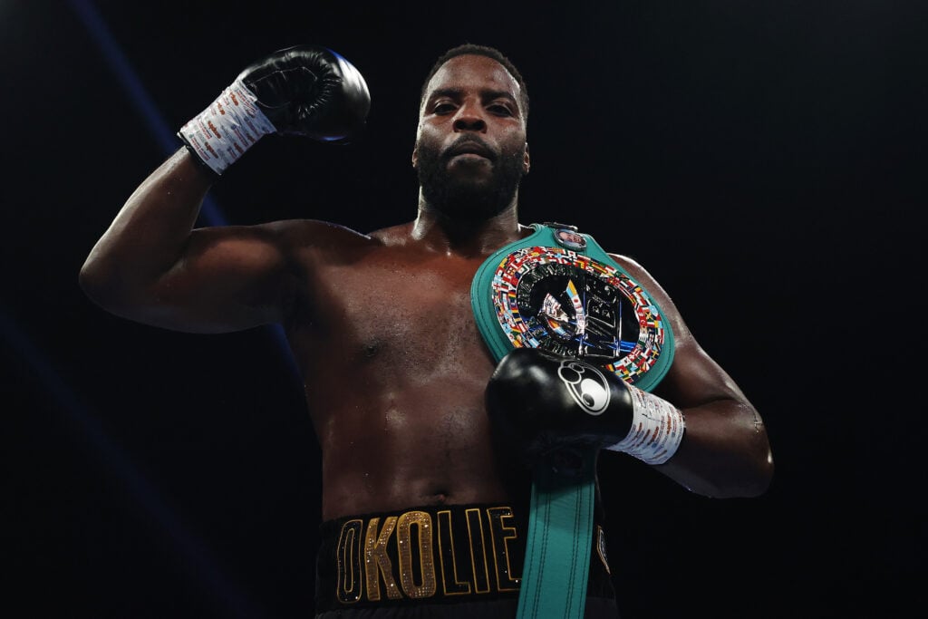 Lawrence Okolie raises an arm with a belt draped over his shoulder to celebrate his heavyweight debut