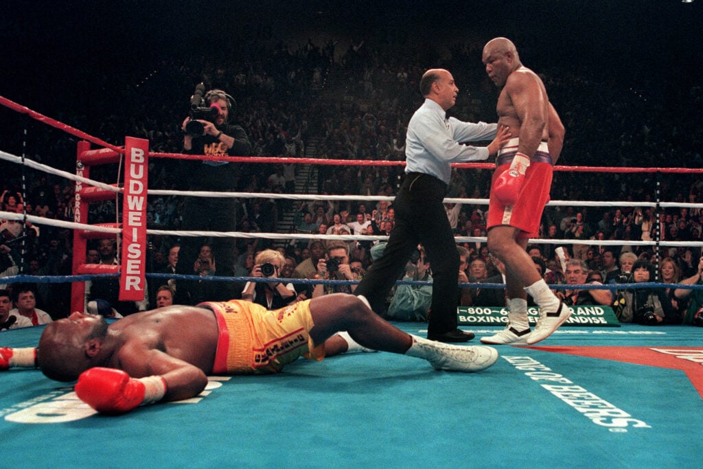 George Foreman looks on as Michael Moorer lays flat in the ring.