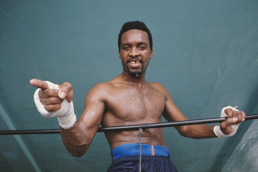 Nigel Benn points at the camera with wraps on in training, he is leaning against ring ropes