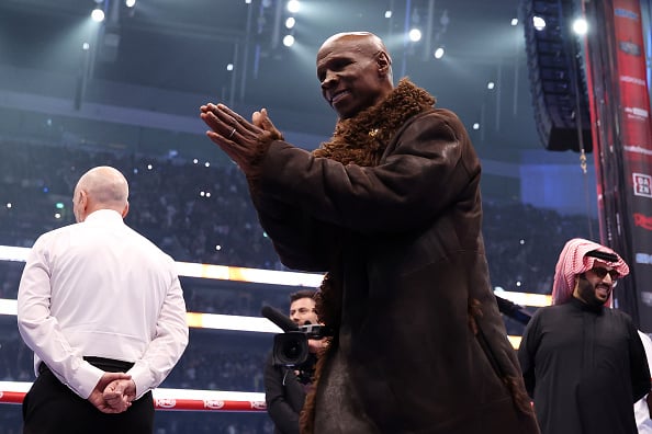 Chris Eubank with fur jacket on clasping his hands together in boxing ring
