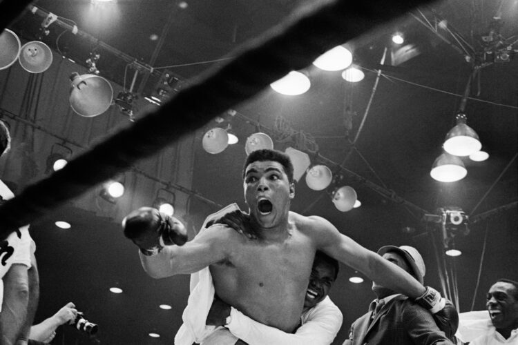 (Original Caption) "I'm the champ!" screams Cassius Clay as his handlers hug him joyfully after he defeated Sonny Liston for the heavyweight boxing...