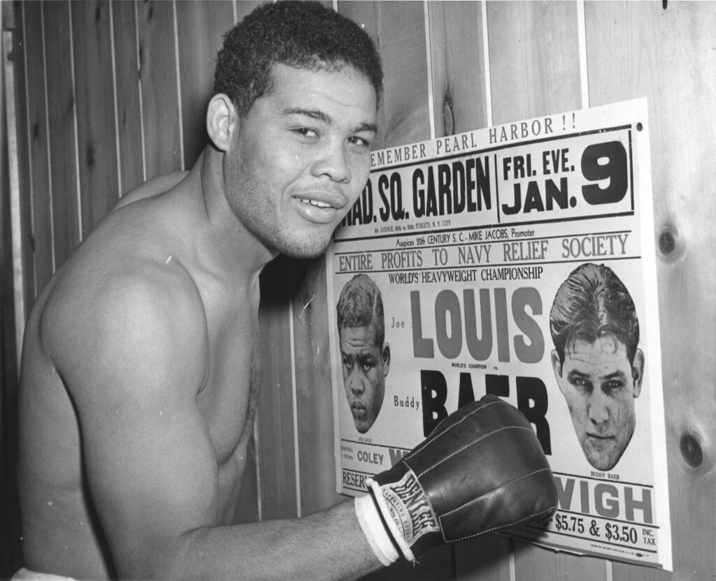 Joe Louis posing with a poster for his fight vs Buddy Baer
