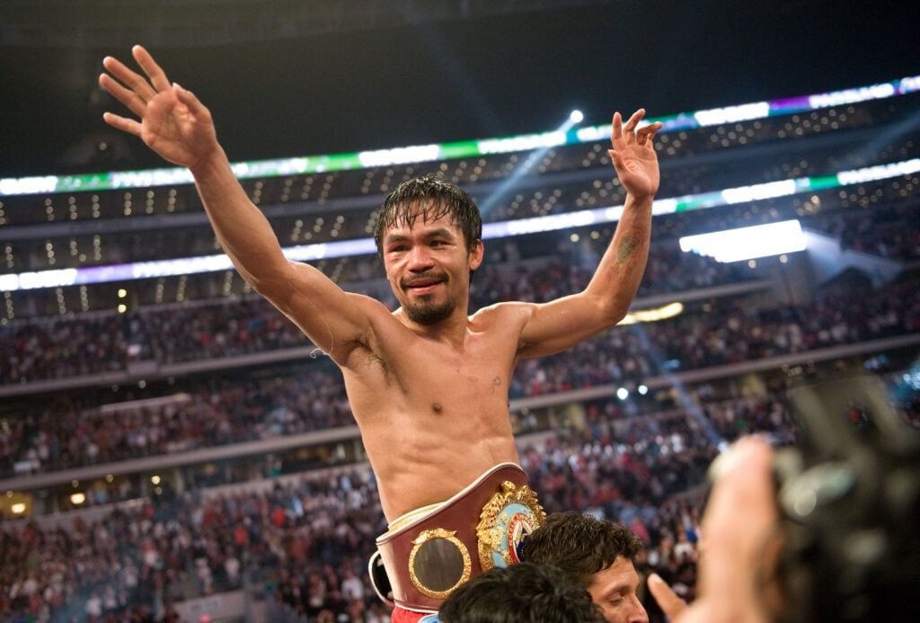 Manny Pacquiao sits upon a teammate's shoulders with a belt around his waist celebrating defeating Joshua Clottey