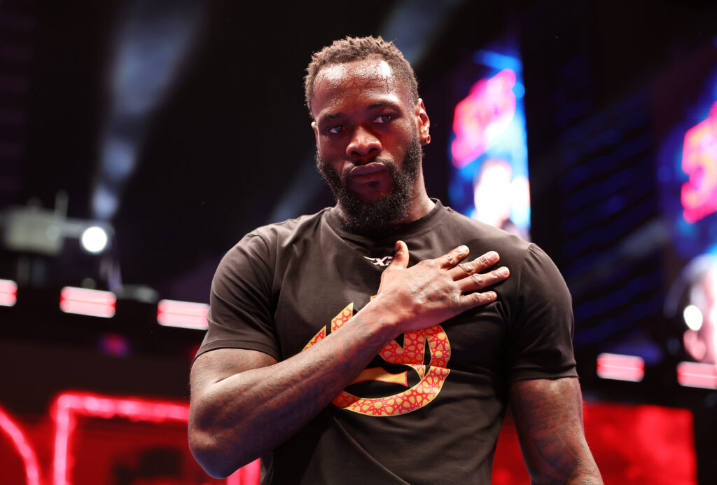 Deontay Wilder stood in the ring wearing a black t-shirt with his hands over his heart at the 5vs5 event in Saudi Arabia